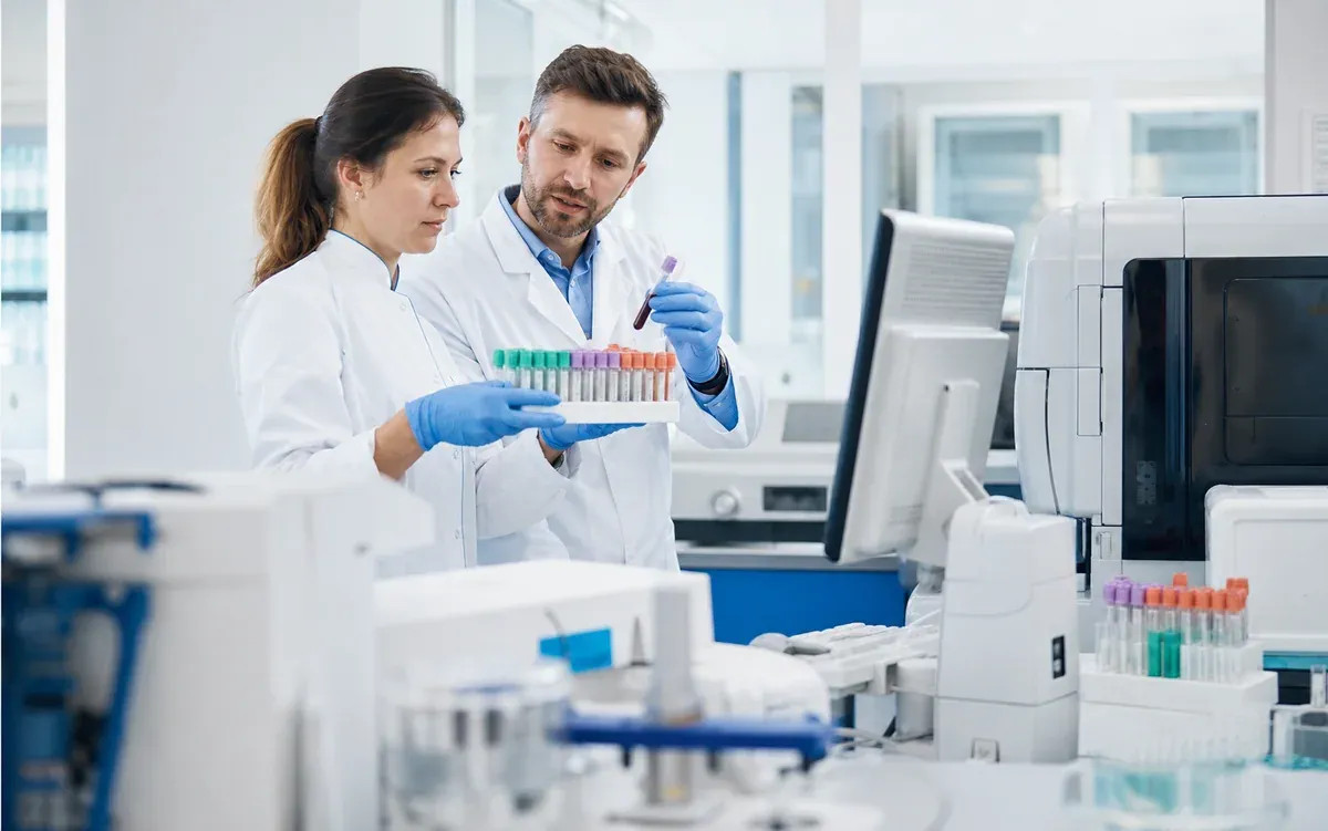 Dwoje naukowców sprawdzających probówki z krwią przy analizatorze laboratoryjnym